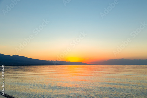 Dawn of the sun at sea. The rising sun behind the mountains. Kyrgyzstan.