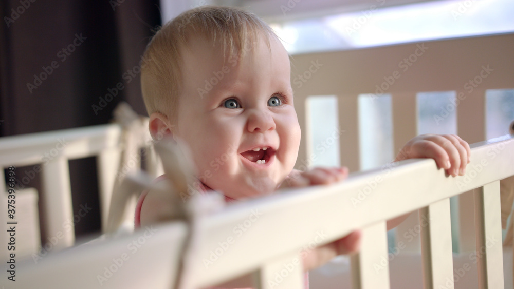 Joyful kid standing in crib. Smiling toddler standing in bed at home