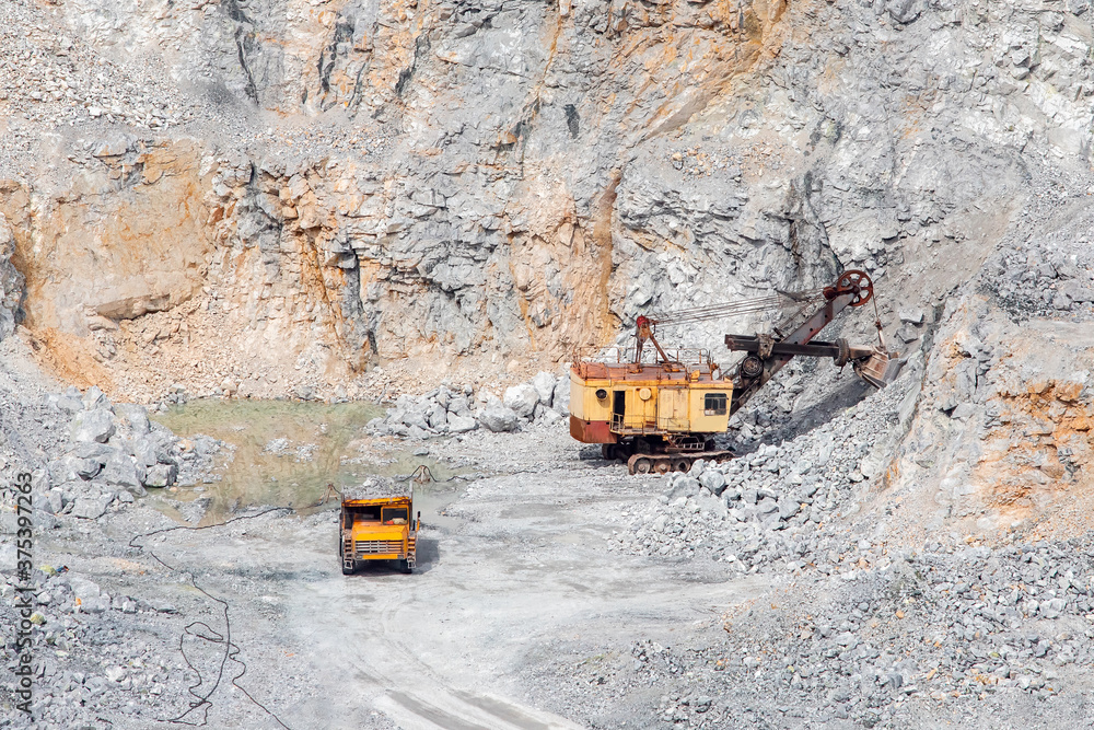Stone open pit mine. Excavator is loading raw materials into yellow truck for transport to combine Stone open pit mine. Excavator is loading raw materials into yellow truck for transport to combine