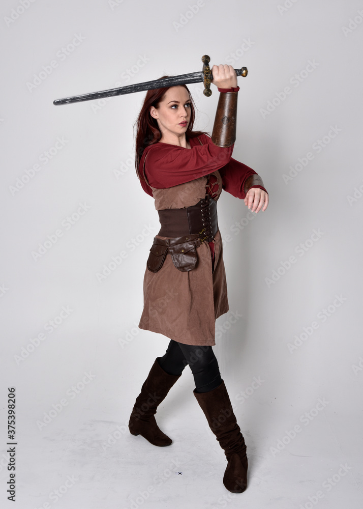 Full length portrait of girl wearing medieval costume. Standing pose holding a sword, isolated against a grey studio background. Full length portrait of girl wearing medieval costume. Standing pose holding a sword, isolated against a grey studio background.