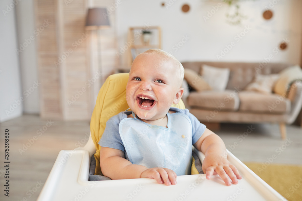 Horizontal portrait of cheerful little child sitting on high chair with food around his mouth smiling at camera, copy space Horizontal portrait of cheerful little child sitting on high chair with food around his mouth smiling at camera, copy space