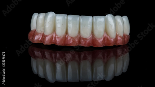 lower jaw prosthesis with artificial red gum and bright white teeth, filmed on black glass with reflection