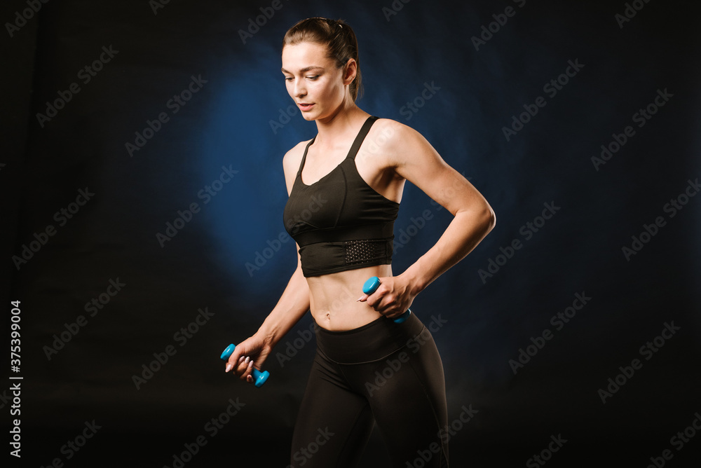 Young, slim girl doing exercises with a dumbbells on black background. Young, slim girl doing exercises with a dumbbells on black background.