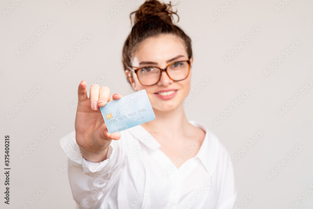 Bank deposit. Business investment. Cheerful woman in white shirt glasses showing credit card smiling isolated on blur neutral copy space background. Cashless payment. Bank deposit. Business investment. Cheerful woman in white shirt glasses showing credit card smiling isolated on blur neutral copy space background. Cashless payment.