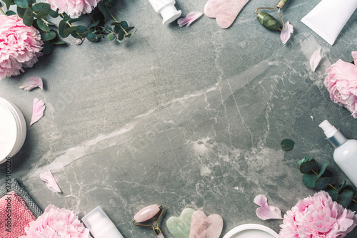 Fototapeta Naklejka Na Ścianę i Meble -  Facial roller, gua sha massager, oil bottle, towel, pink peonies on marble background. Copy space. Flat lay. Top view. Routine facial skin care, body treatment, spa concept.