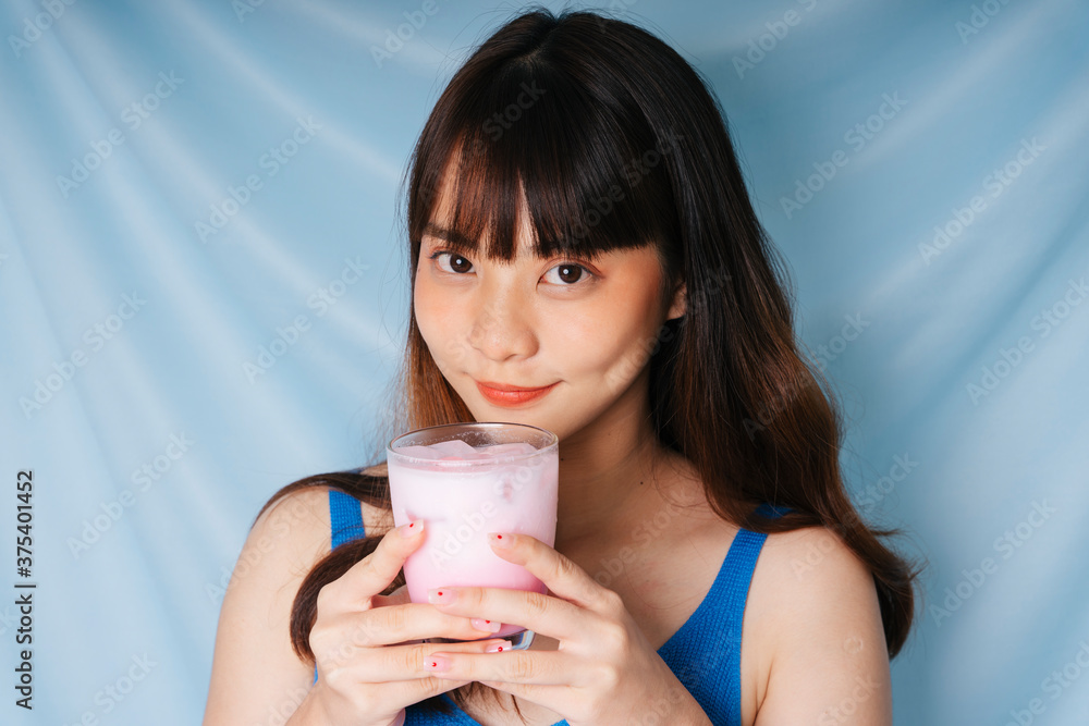 Young asian dark hair woman holding glass of pink milk shake with both hands. Young asian dark hair woman holding glass of pink milk shake with both hands.