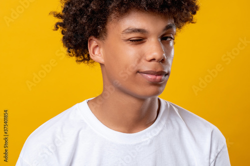Black teenager portrait. Positive mood. Smiling african male student looking at camera winking. Isolated on orange copy space. Ethnic tolerance. Confidence success. Advertising background
