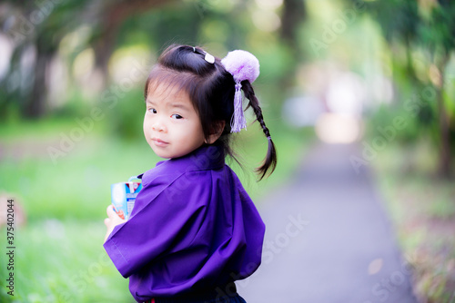 Adorable girl standing holding milk carton box and leaned over looking at camera behind her. Student wearing a purple school uniform, it was a gym uniform. Sweet smiley girl, age 3 and half years old.
