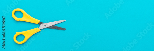 Minimalist photo of yellow children's scissors on the turquoise blue background. Flat lay shot of opened yellow scissors with copy space.