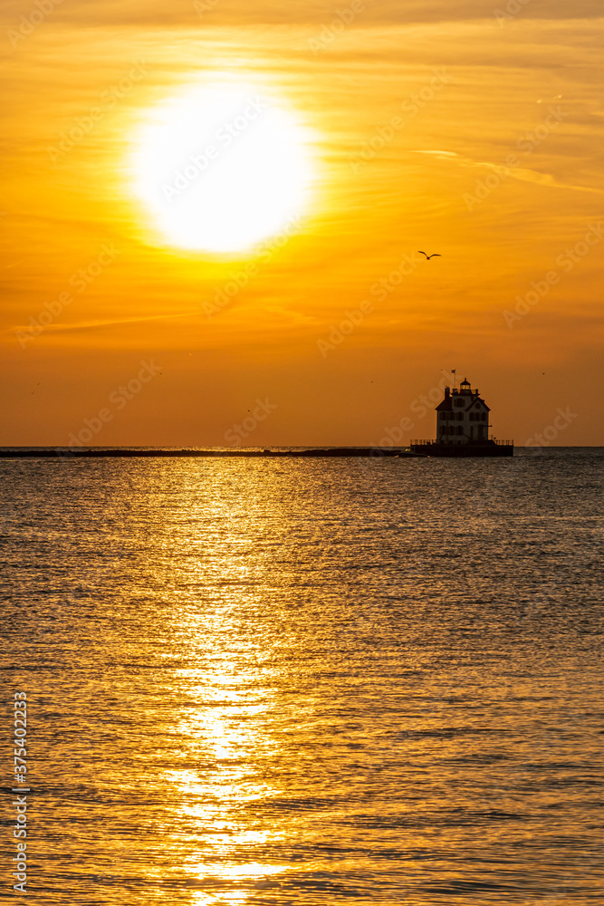 Orange sunset over historic lighthouse in calm water of bay Orange sunset over historic lighthouse in calm water of bay