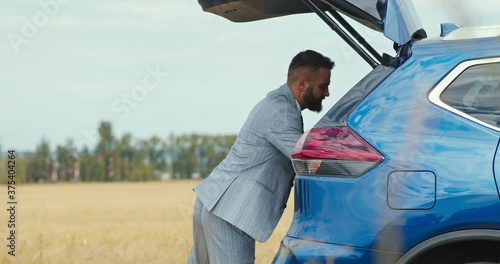 Businessman putting his sport bag into car trunk and closing it by pushing the button, countryside shot photo