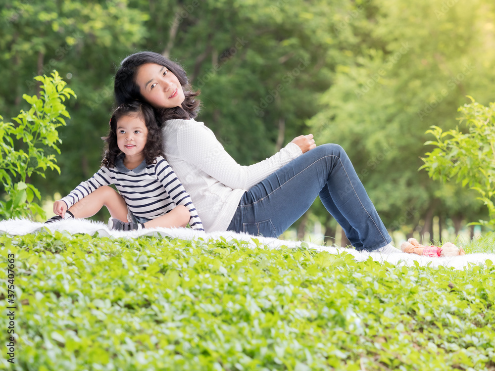 Asian little girl sitting with her mom on the carpet, Relax and learning outside of school to enjoy in the nature park Asian little girl sitting with her mom on the carpet, Relax and learning outside of school to enjoy in the nature park