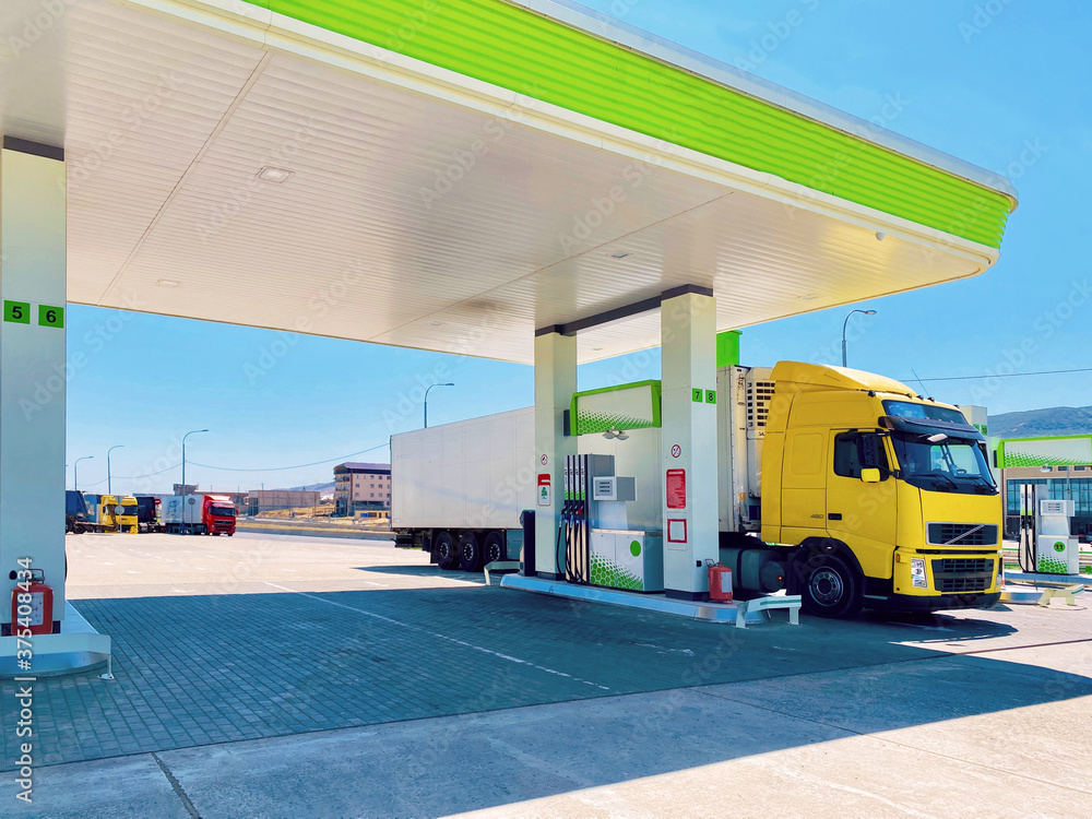 bright yellow truck with refrigerated semi-trailer at the fuel stop for refueling