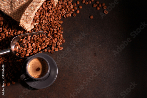 Grey cup and brown coffee beans in metal scoop scattered from burlap bag and dark table background with copy space. Arabica grains, top view. Coffee shop, caffeine, roast concept