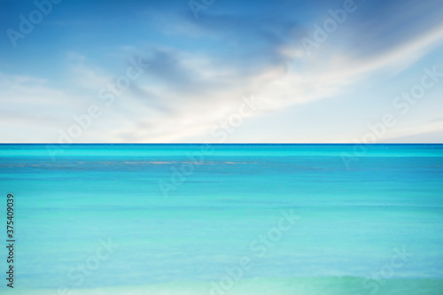 Blue sea against blurry sky with soft clouds summer background
