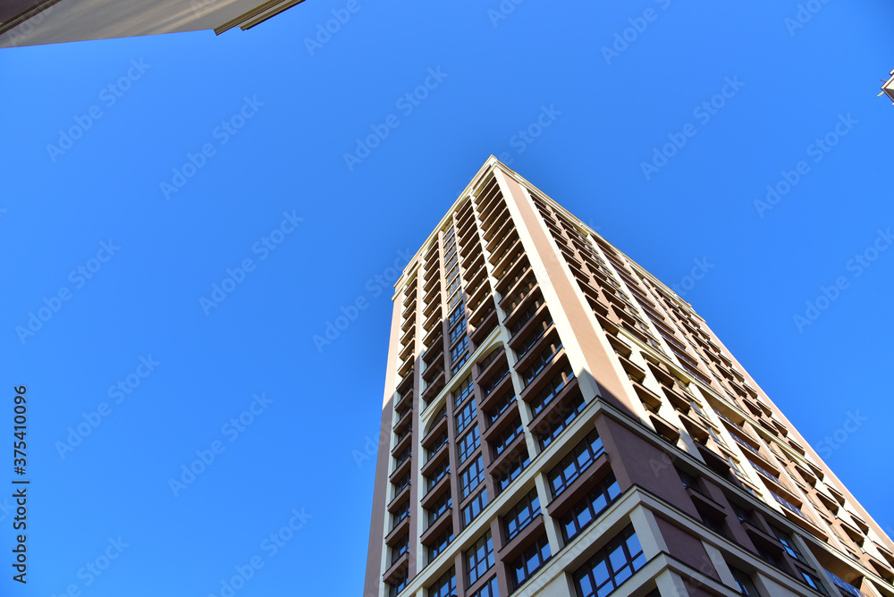 Facade of a new modern high-rise residential building. Skyscraper on blue sky background. Tall house renovation project, government programs. Minimalistic multi storied home. Urban architecture