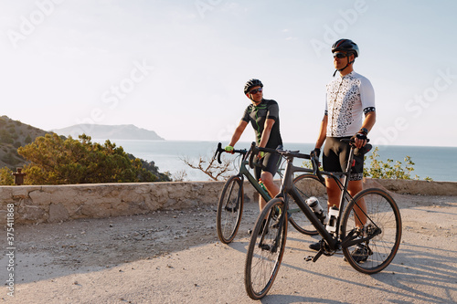 Two male cyclists stand on the road and have a rest