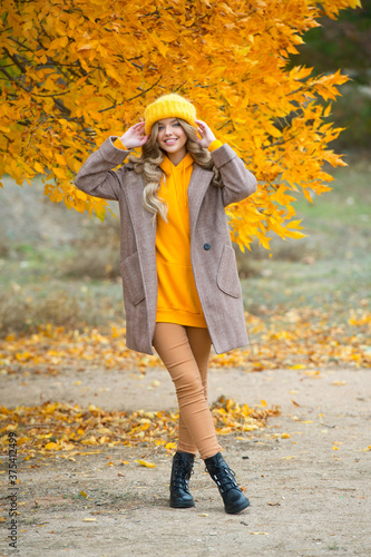 Beautiful woman walking outdoors in autumn. Smiling woman collects yellow leaves in autumn. Young woman enjoying autumn weather.