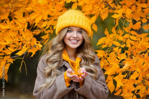 Beautiful woman walking outdoors in autumn. Smiling woman collects yellow leaves in autumn. Young woman enjoying autumn weather.