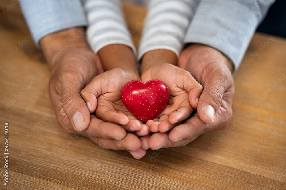 Man and child hand holding red heart stone Man and child hand holding red heart stone