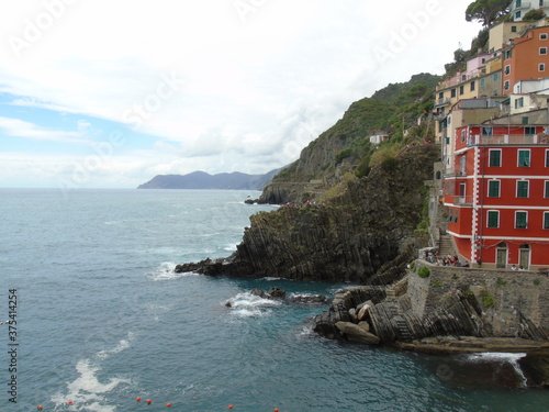 Riomaggiore, Italy - 08/31/2020: Beautiful photography of the countryside from Cinque Terre, Italy. Grey sky, colourful houses, grape coltivation from the mountains, and some small waves from the sea.