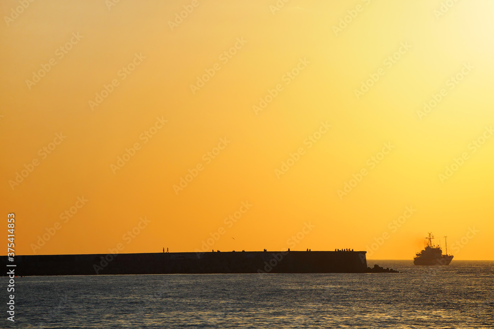 Orange sunset on the sea. Sky and sea background Silhouettes of people and a ship at the sea pier