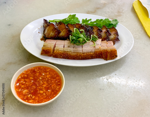 Crispy Roasted Crackling Pork Belly in Chinese Cantonese cuisine called Siu Yuk, fresh herbs, chili garlic dipping sauce, white plate, marble table top.  (ID: 375414888)
