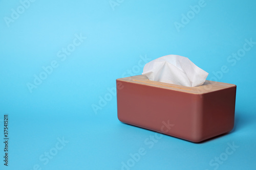 Holder with paper tissues on light blue background. Space for text