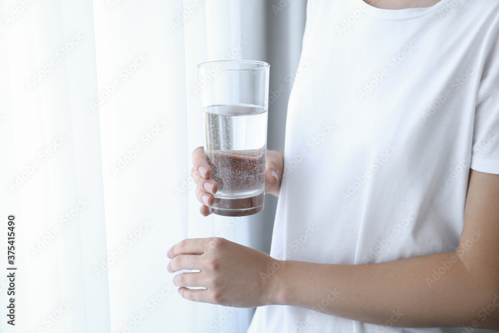 Woman holding glass of water near window at home, closeup Woman holding glass of water near window at home, closeup