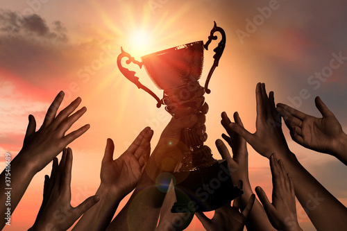 Winning team with gold trophy cup against shining sun in sky