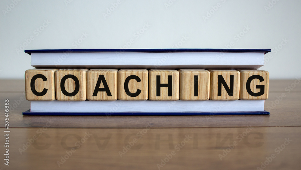 Concept word 'coaching' on wooden cubes between pages of a book on a beautiful wooden table. White background. Business concept. Copy space.