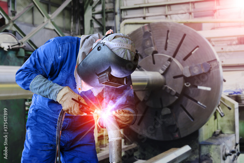 Workers welder welding by Tig gas argon on steel pipe line fabrication in factory on old lathe is on the background.