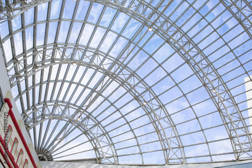 A metal structure supporting the supermarket glass dome. Transparent ceiling letting in sunlight, glass dome blue sky. Modern trendy building architecture