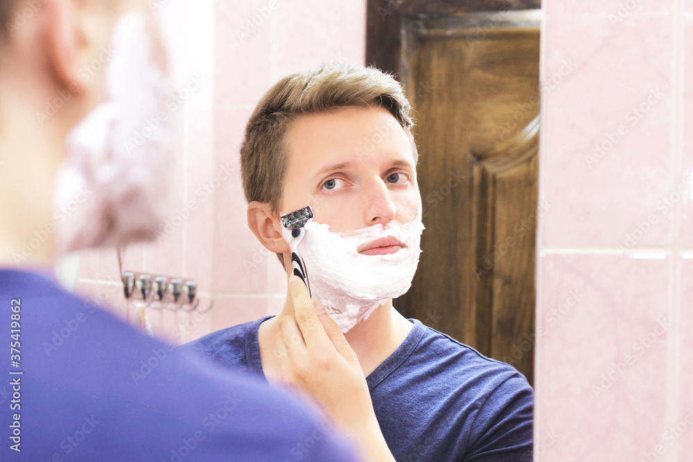 A guy shaves in front of a mirror. Facial care. Razor and foam