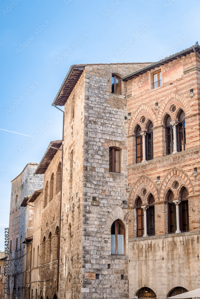 Medieval building with windows in the Venetian style on the central square Piazza Della Cisterna in San Gimignano, Italy