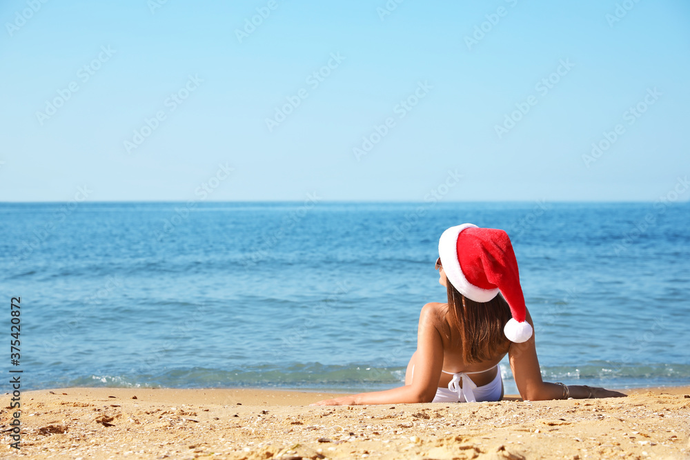 Young woman wearing Santa hat and bikini on beach, space for text. Christmas vacation Young woman wearing Santa hat and bikini on beach, space for text. Christmas vacation