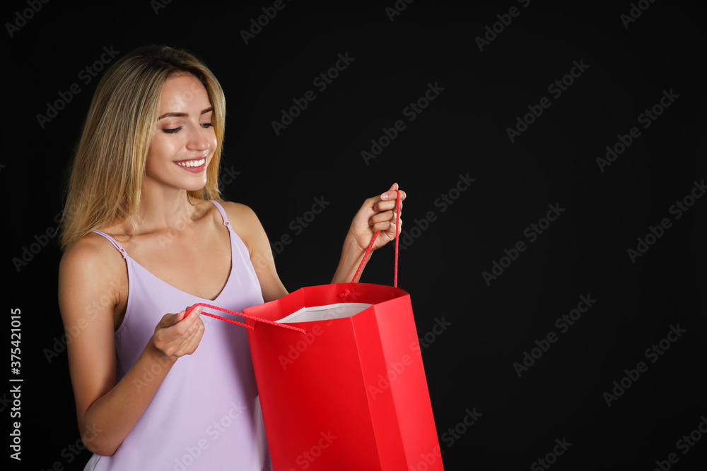 Happy young woman with shopping bag on dark background, space for text. Black Friday Sale Happy young woman with shopping bag on dark background, space for text. Black Friday Sale