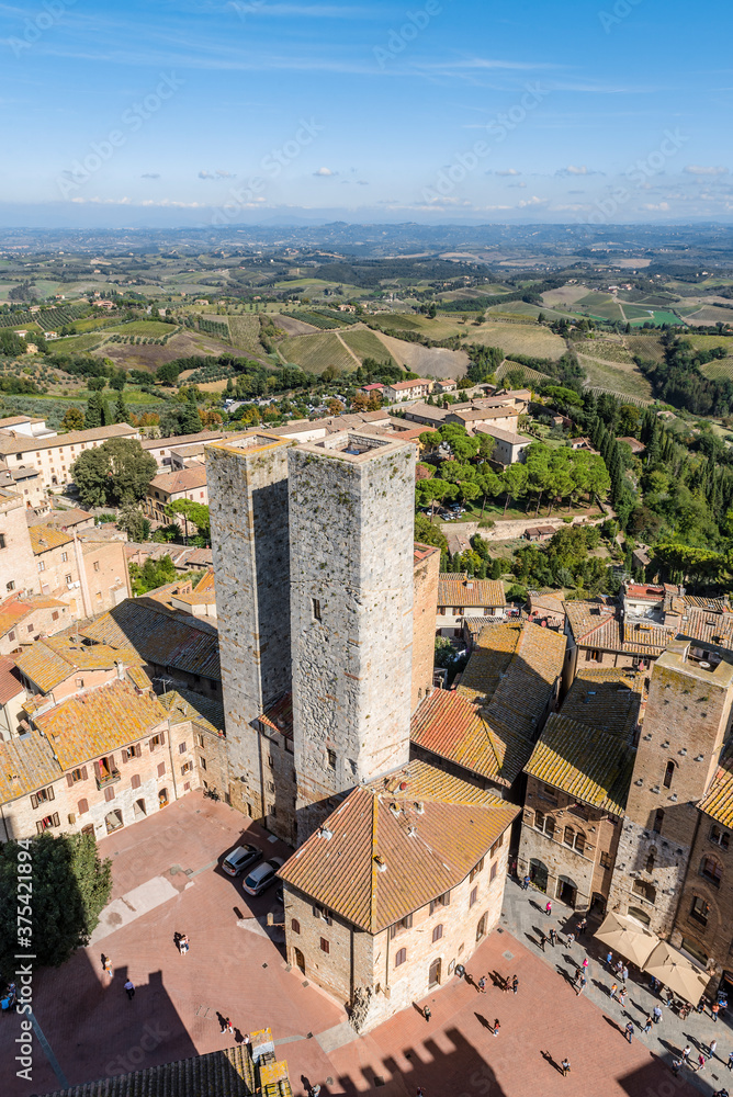 Aerial view of the medieval houses, central sqare and towers of San Gimignano, Italy, and the surrounding fields, forests and mountains
