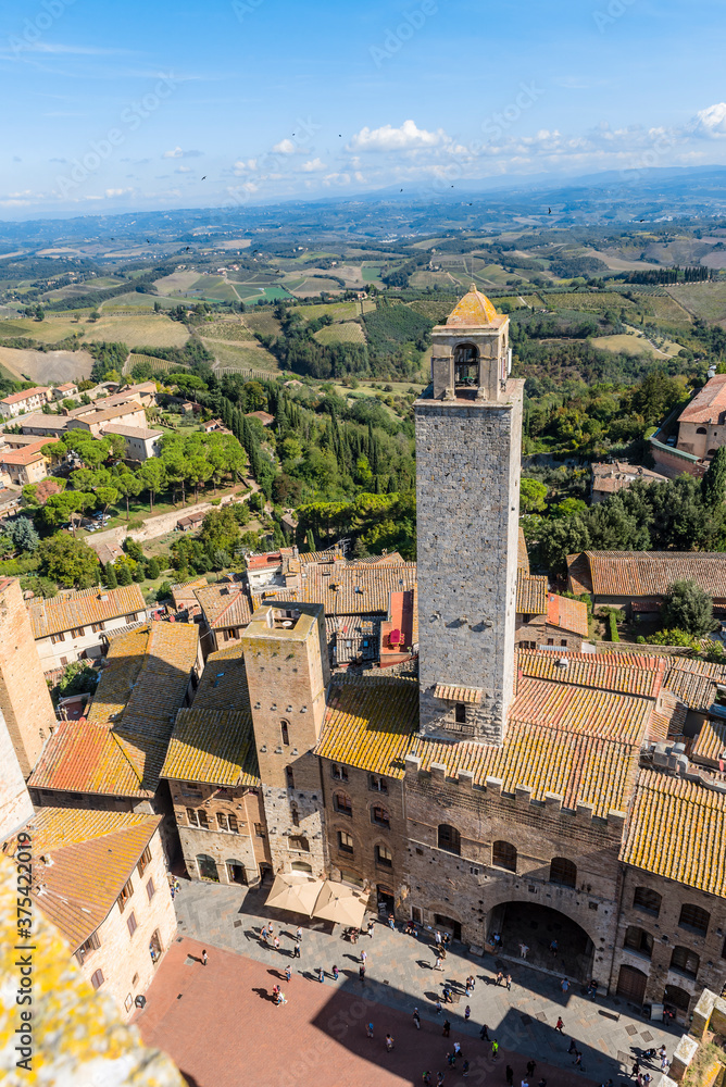 Aerial view of the medieval houses, central square and towers of San Gimignano, Italy, and the surrounding fields, forests and mountains