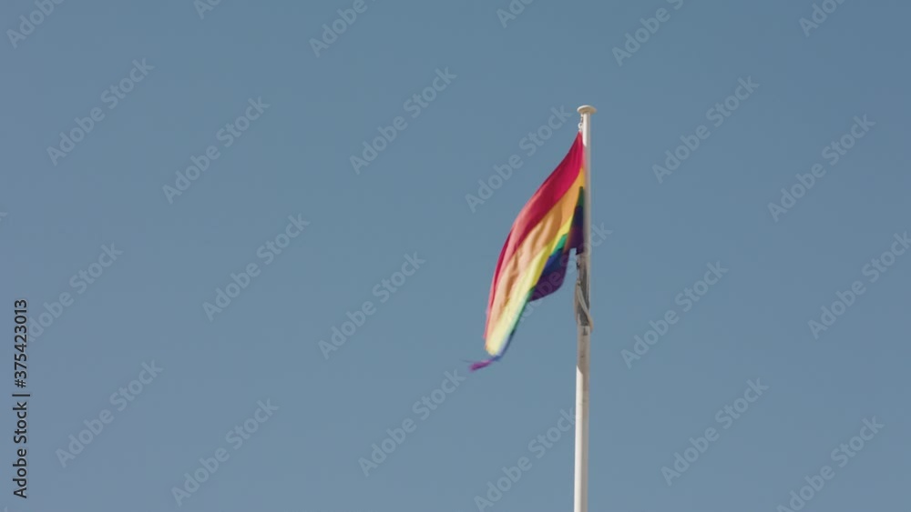A rainbow pride flag flaps in the wind on a blue sky summer day A rainbow pride flag flaps in the wind on a blue sky summer day