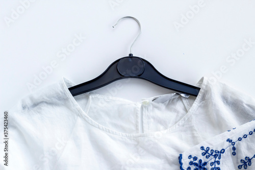 Blue embroidered on white ladies summer blouse on white surface with blouse hanger