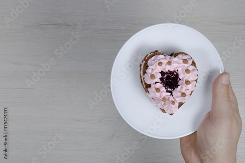 Heart shaped cake in hand on a background of bleached wood.