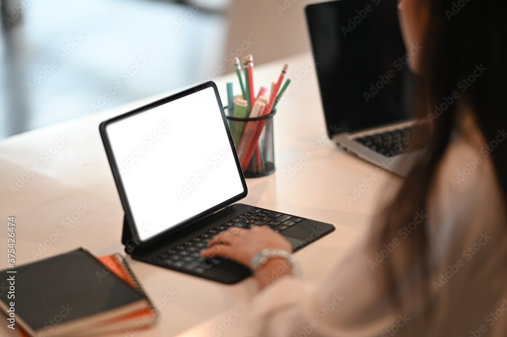 Cropped image of a woman is using a computer tablet while sitting at the white working desk. Cropped image of a woman is using a computer tablet while sitting at the white working desk.