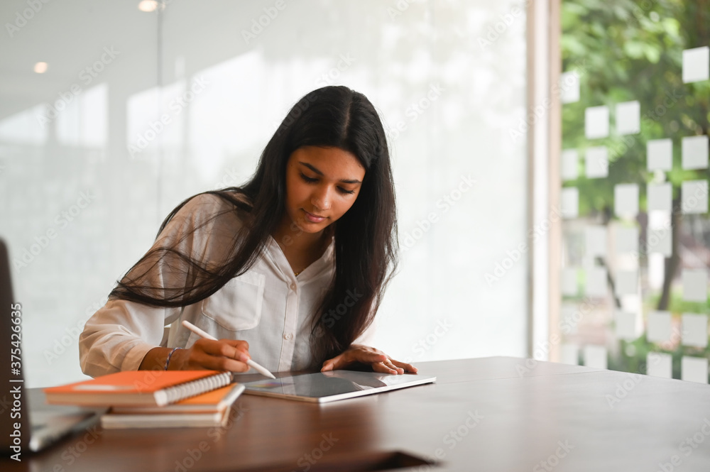 A beautiful woman is sketching on a computer tablet at the wooden working desk. A beautiful woman is sketching on a computer tablet at the wooden working desk.