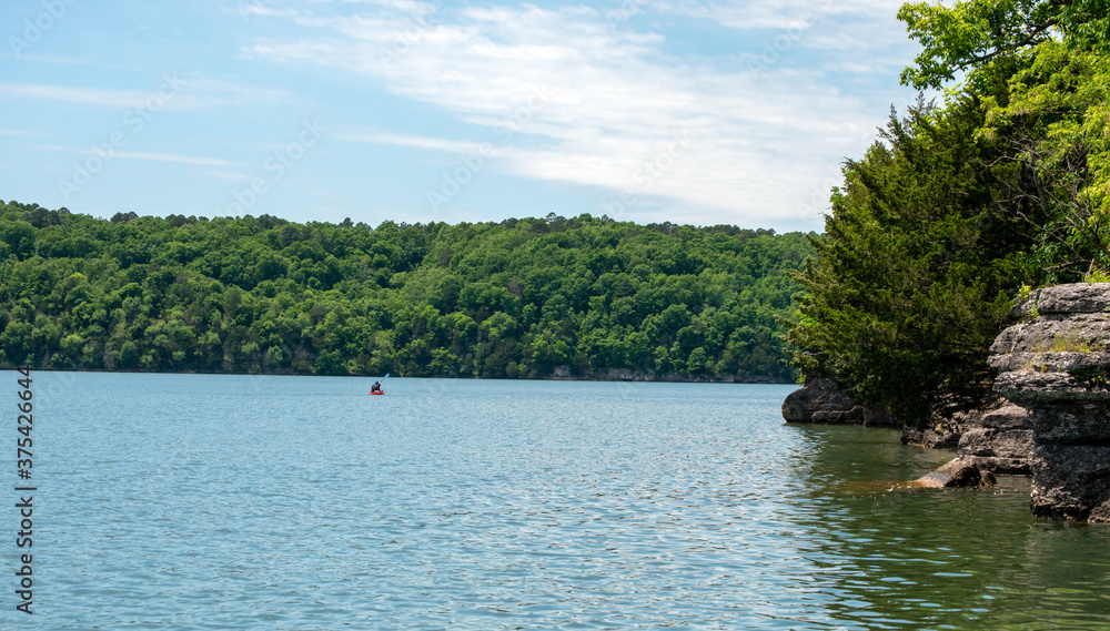 An unidentified person enjoys a peaceful day of calm kayaking on a beautiful scenic lake in Oklahoma, Bokeh effect.