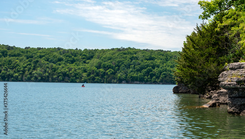 An unidentified person enjoys a peaceful day of calm kayaking on a beautiful scenic lake in Oklahoma, Bokeh effect.