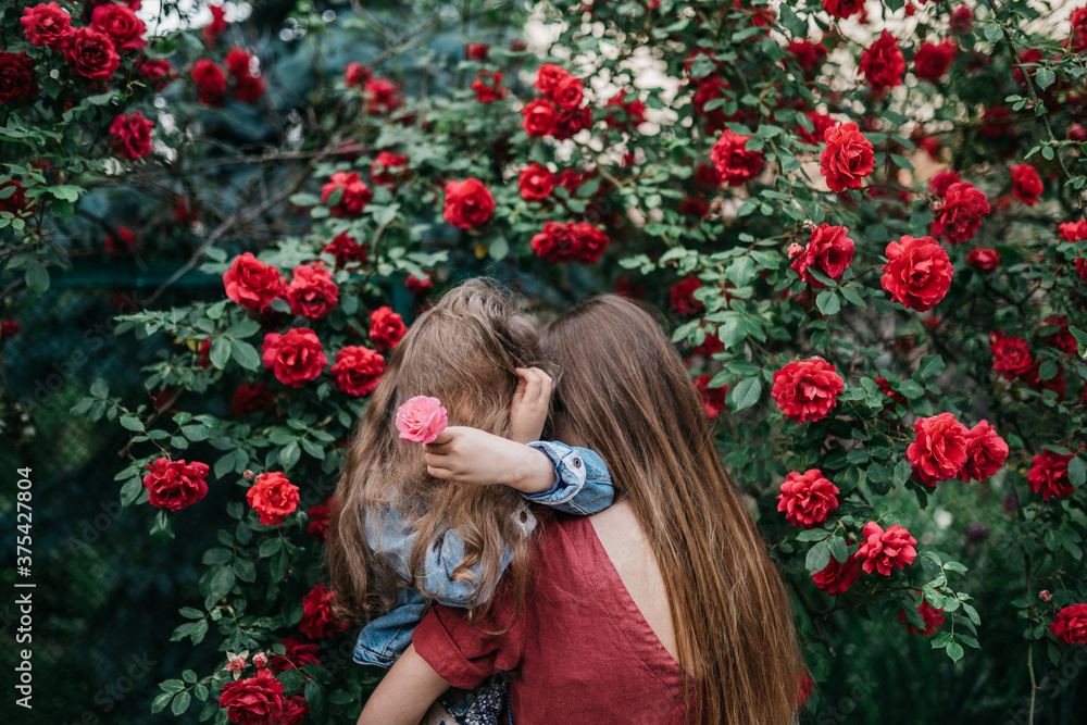 Naklejka premium upset daughter in her mother's arms is hiding from society and is looking for support in the park near red roses.
