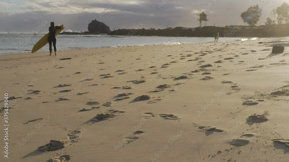 Female Surfer With Surfboard Leaving The Beach After Enjoying The Waves