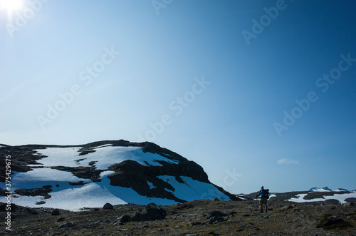 Hiking in Swedish Lapland. Man traveler trekking alone Nordkalottruta Arctic Trail in northern Sweden. Mountain nature of Scandinavia in summer sunny day photo against sun with space for text photo