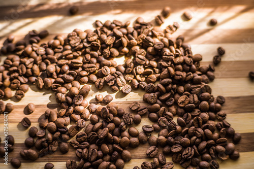 Roasted arabica coffee beans are scattered on a wooden plank.